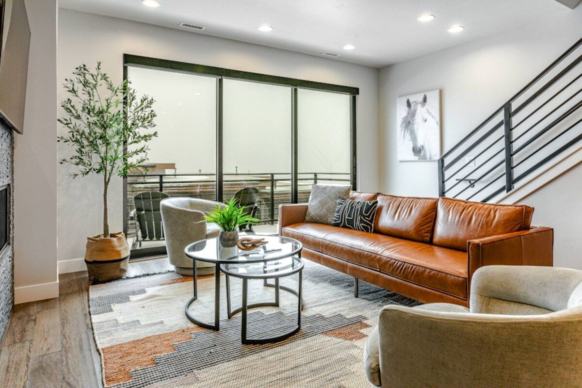 Una sala moderna con un sofá de cuero, una mesa de centro de vidrio y vistas a un balcón a través de amplios ventanales.