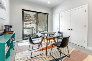 A modern dining area with a glass table and chairs, a teal-colored cabinet, and a view of a snowy outdoor area through a sliding glass door.