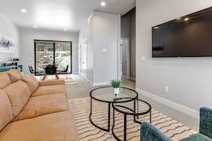 A modern living room with a sectional sofa, a glass coffee table, and a flat-screen TV mounted on the wall.