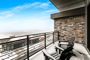 A balcony with a stone wall, a metal railing, and two Adirondack chairs.