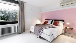 Quarto com cama, mesa de cabeceira e janela com cortinas.