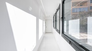 Um corredor com grandes janelas, piso branco e uma porta no final.