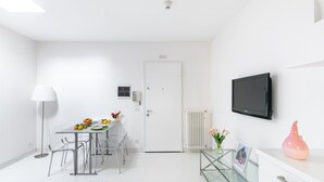 Quarto moderno e bem iluminado com uma mesa de jantar, cadeiras, luminária, televisão e radiador.