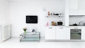 Uma cozinha moderna com armários brancos, uma mesa de vidro, uma TV de tela plana e um forno embutido.