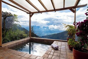 Piscina infinita con paredes de vidrio y vistas a montañas y nubes.