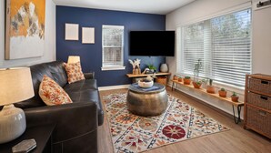 A living room with a dark leather sofa, a round coffee table, a patterned rug, a flat-screen TV, and a window with blinds. - Top 5%  - Finnish Sauna - Near Old Mill - No Pets - Fully Remodeled - Quiet (Bend)