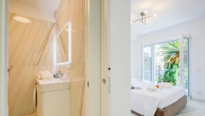 Un baño moderno con tocador de mármol y zona de ducha. La habitación cuenta con un ventanal con vistas a zonas verdes.