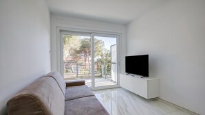 Una sala de estar con un sofá, un televisor sobre un mueble blanco y un ventanal corredizo que da a un espacio exterior.