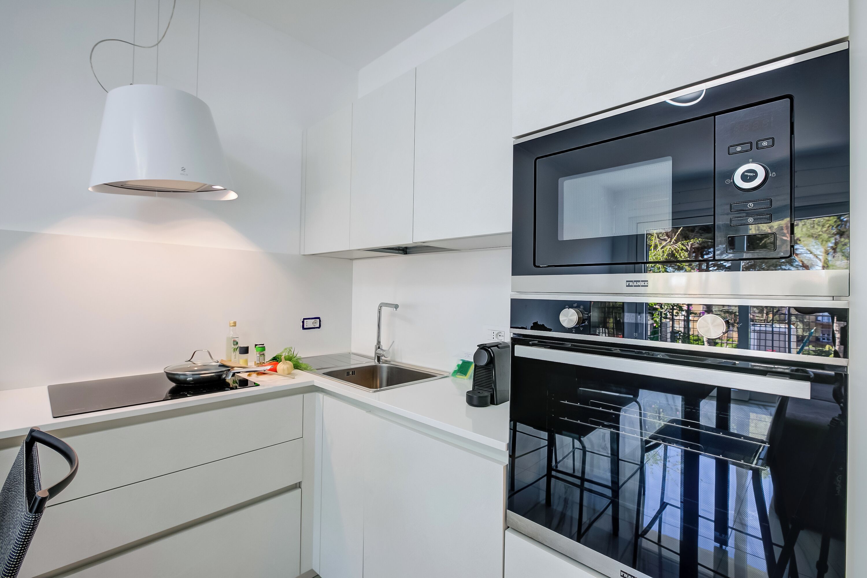 A modern kitchen with white cabinetry, a built-in oven, a microwave, and a hanging light fixture.