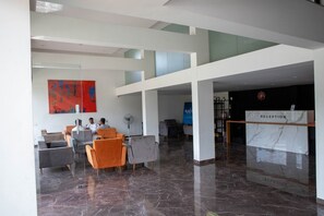 Una hall d'albergo moderna con pavimento in marmo, una reception, aree salotto e un grande quadro astratto.