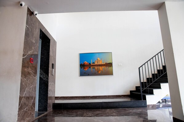 Un interno moderno con una scala in marmo, un quadro incorniciato di un monumento famoso e una telecamera di sicurezza.
