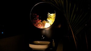 Un bagno con uno specchio rotondo che riflette una pianta e un lavabo.