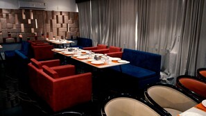 Un ristorante con sedute rosse e blu, tavoli apparecchiati con piatti e bicchieri, e un design moderno delle pareti.