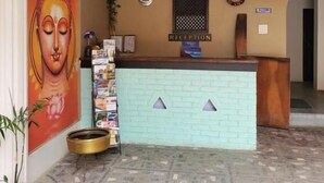 A reception area with a light blue brick wall, a reception desk, a large Buddha mural, a clock, and a sign indicating the reception. - Gauthali Ghar The Swallow Home (Kathmandu)