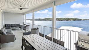 A covered outdoor area with a view of a lake, furnished with a sofa, chairs, and a table.