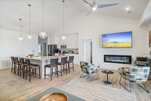 Una cocina moderna con una isla central, taburetes de bar, iluminación colgante y una chimenea.