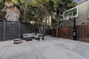 Patio trasero con aro de baloncesto, mobiliario exterior y valla de madera.