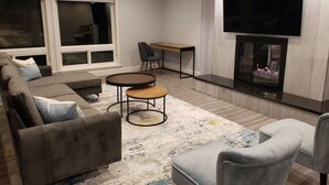 Uma sala de estar com sofá, duas poltronas, uma mesa de centro, televisão e lareira.