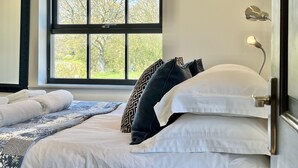 Een net opgemaakt bed met witte en donkere kussens, een geborduurde plaid en een bedlampje.