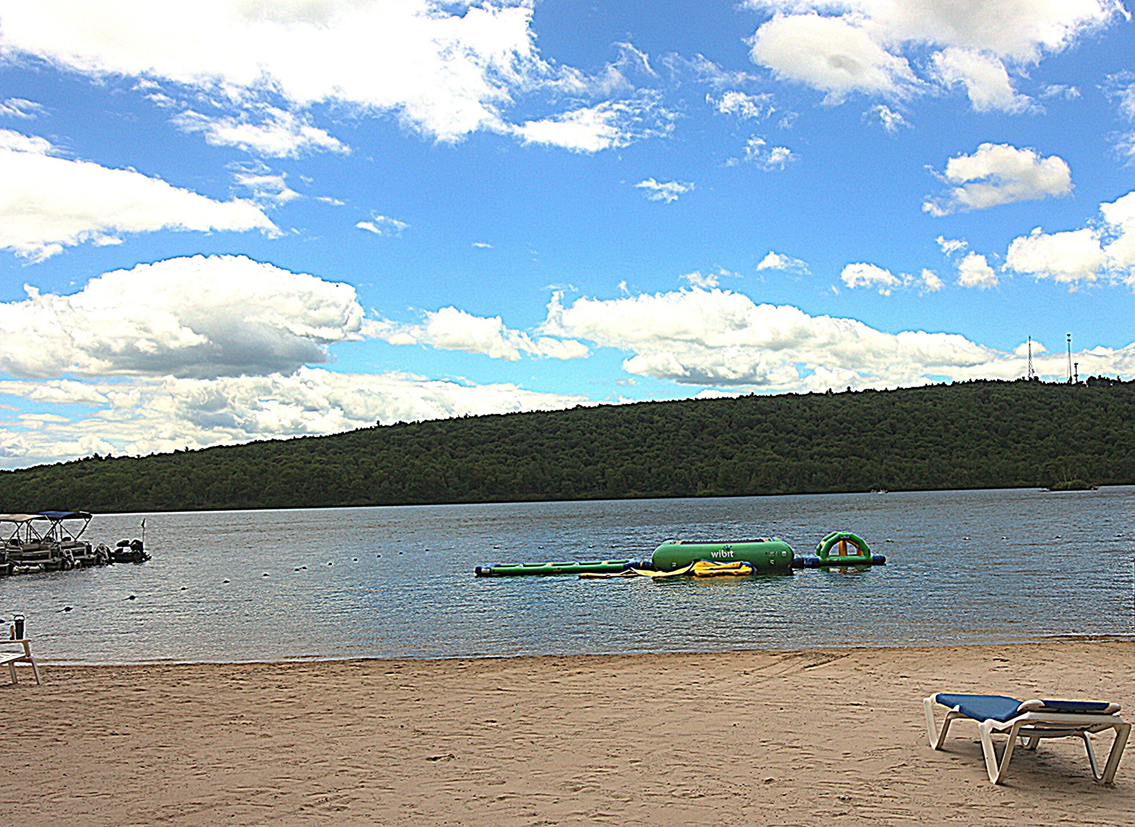 Une vue sur le lac, avec une plage de sable, un bateau à rames et une rangée de chaises de plage.