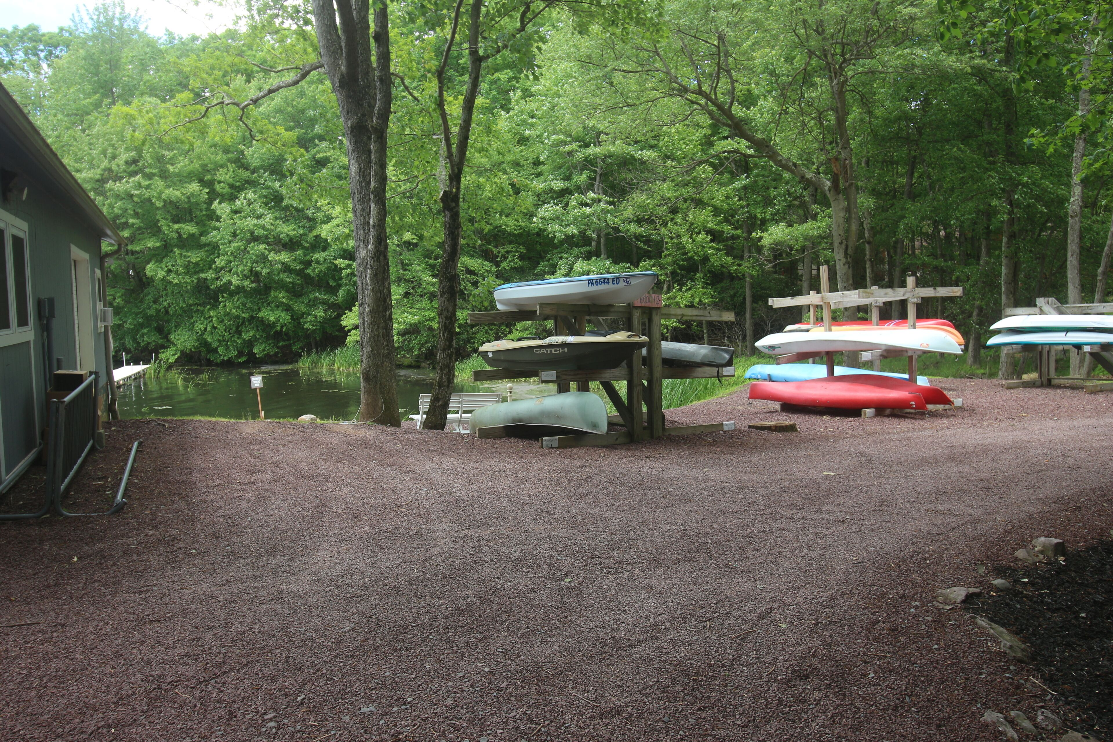 A gravel area with several canoes and kayaks parked on wooden racks.