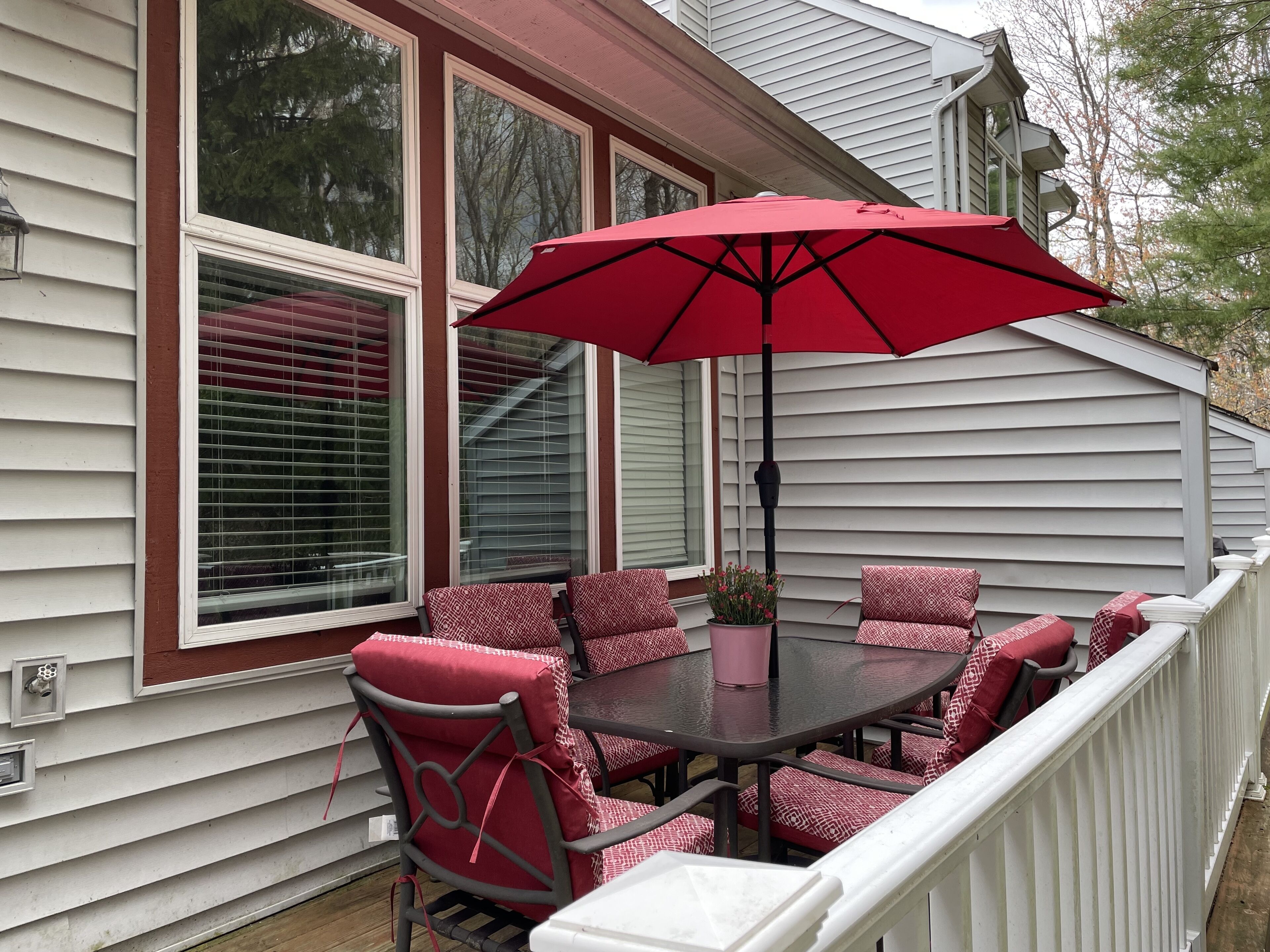 A covered outdoor seating area with a table and chairs, a red umbrella, and a potted plant.