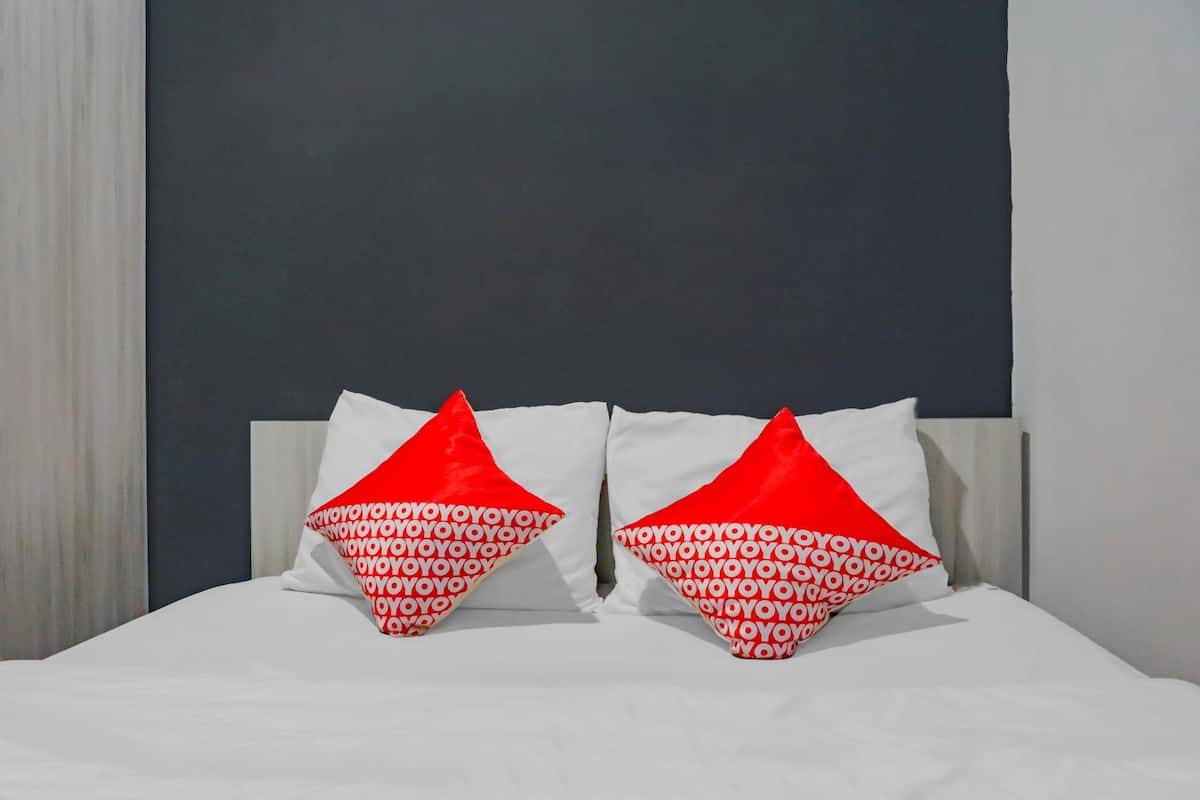 Ein Bett mit weißer Bettwäsche und zwei roten Kissen mit einem sich wiederholenden Muster.