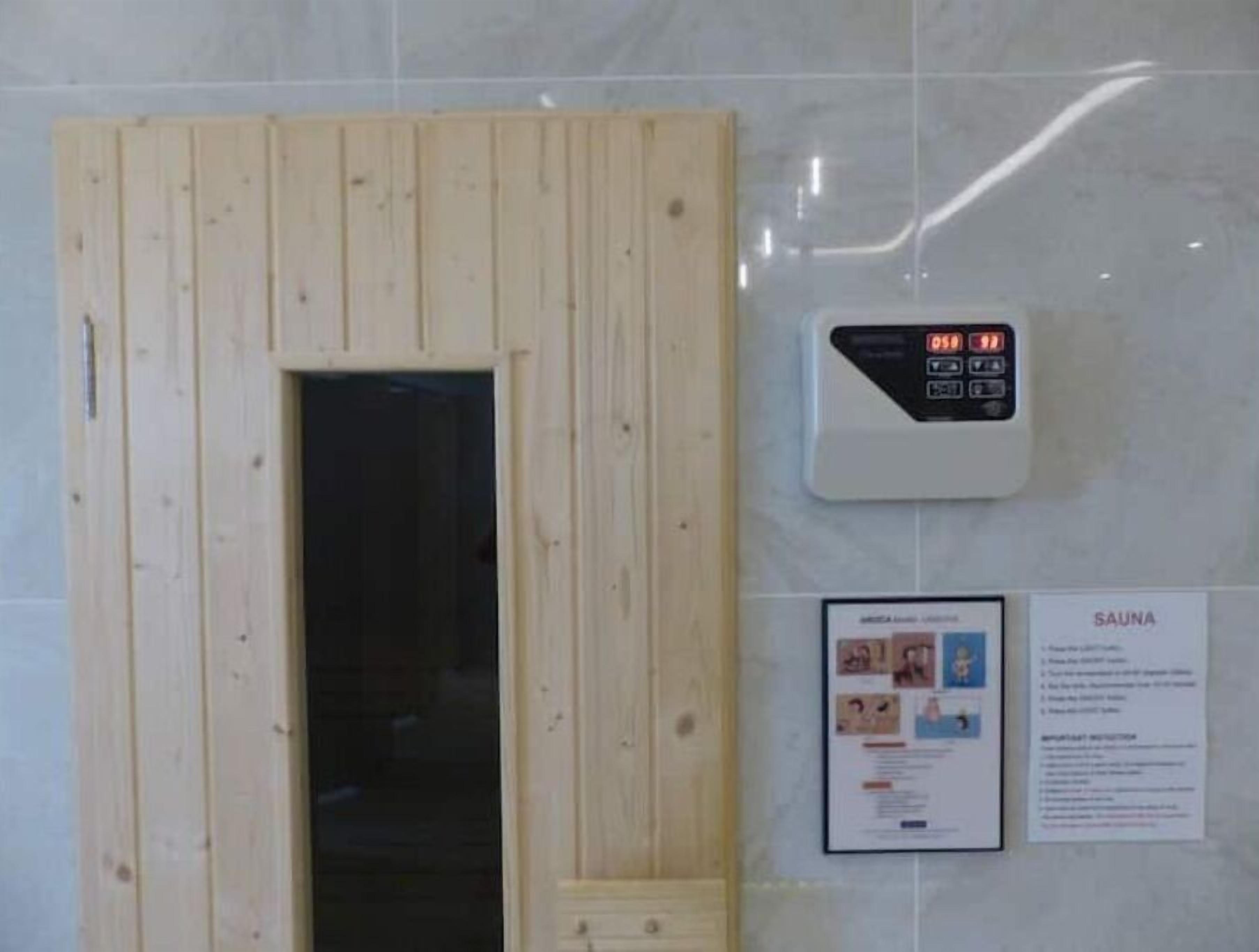 Een sauna met een houten deur, een digitaal bedieningspaneel en informatieposters aan de wand.