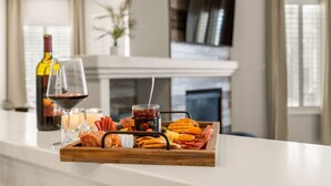 A wooden tray with snacks and a bottle of wine on a white countertop in a modern kitchen with a fireplace in the background. - Family Friendly Game House BBQ Pool Table Tahoe (Reno)