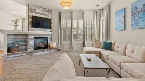 A modern living room with a fireplace, a sofa, a coffee table, and a large window with shutters. - Family Friendly Game House BBQ Pool Table Tahoe (Reno)