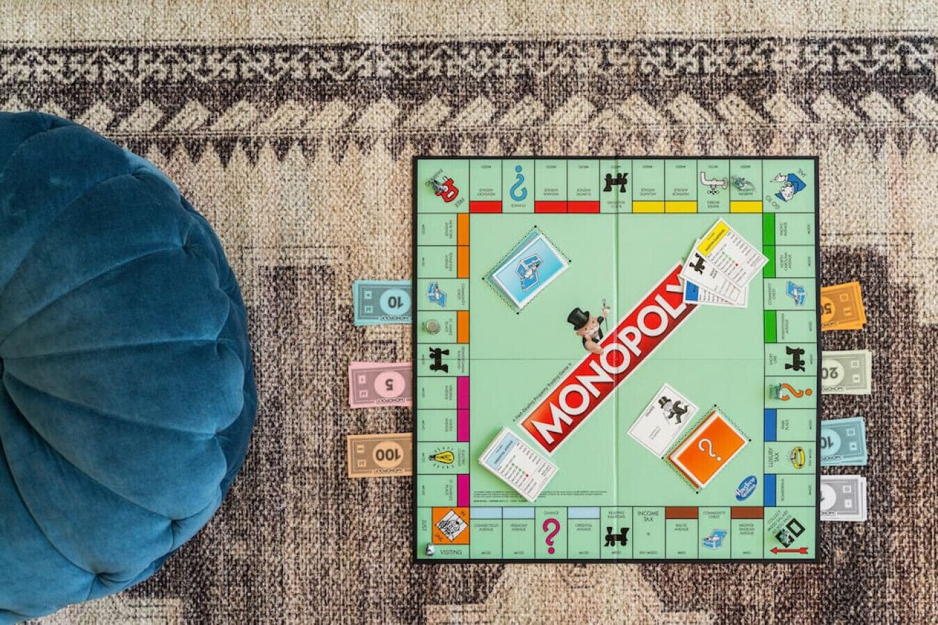 Un juego de mesa Monopoly sobre una alfombra, con un cojín azul con textura cerca.