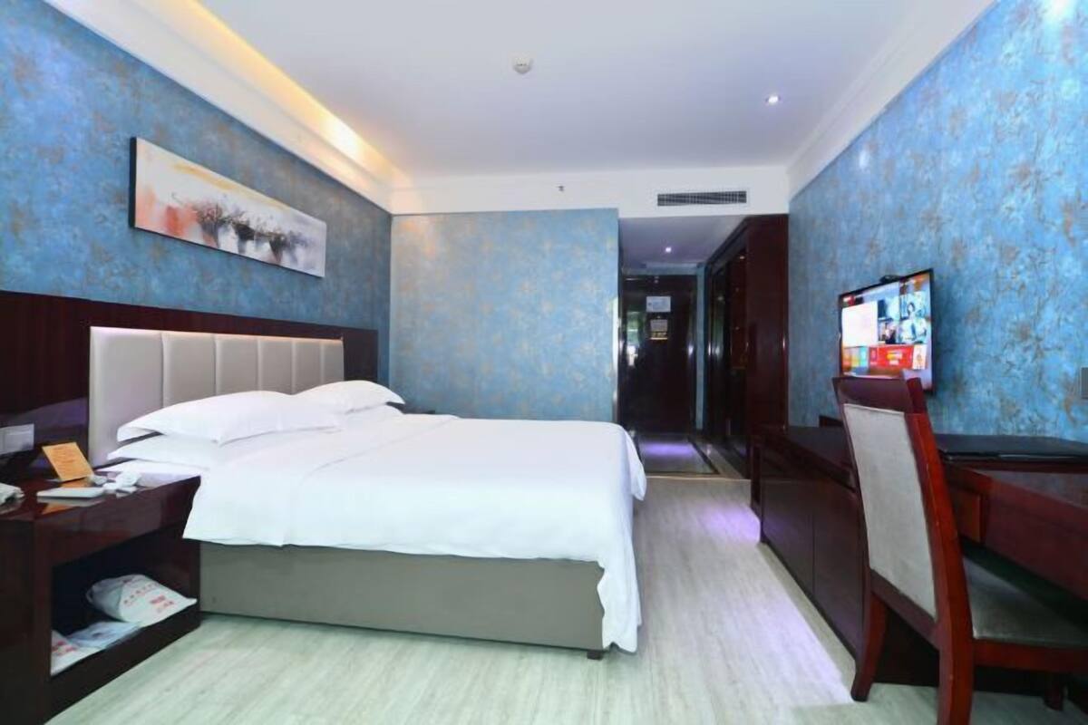 Une chambre d’hôtel avec un grand lit, un bureau, une chaise, une télévision et un tableau au mur.