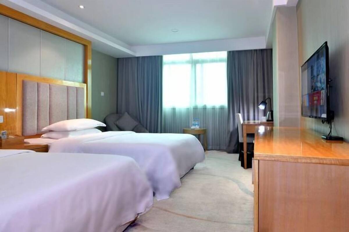 Une chambre d’hôtel avec deux lits, un bureau, une télévision et une grande fenêtre avec des rideaux.