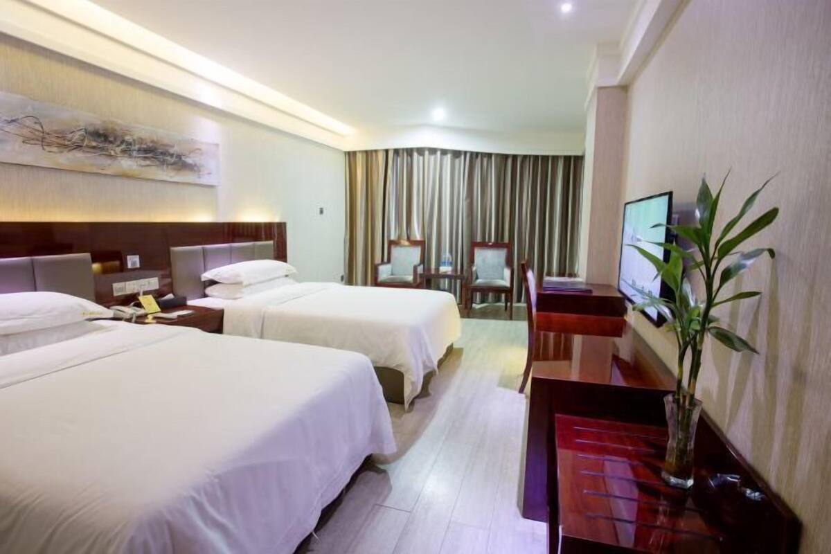 Une chambre d’hôtel avec deux lits, un bureau, une chaise, une télévision et une plante.