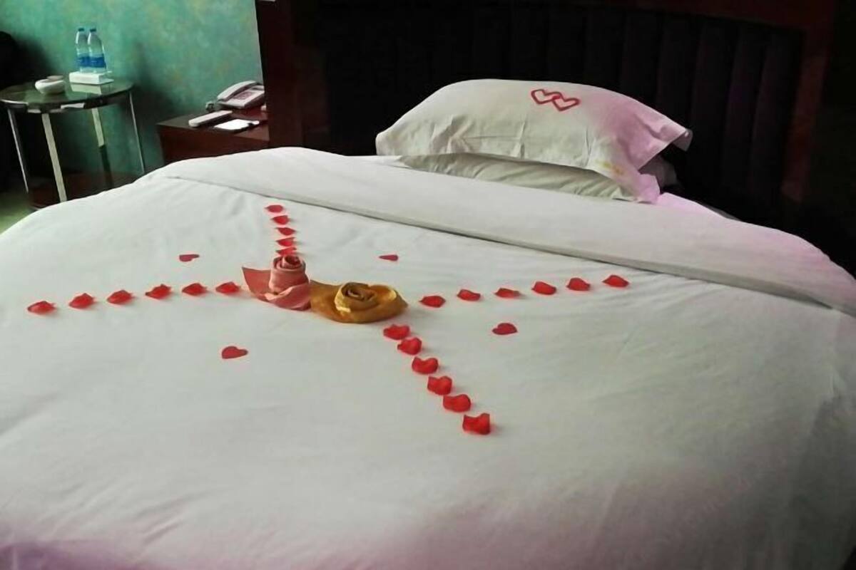 Un lit soigneusement fait, parsemé de pétales de rose disposés en forme de cœur, avec un petit objet doré placé au centre.