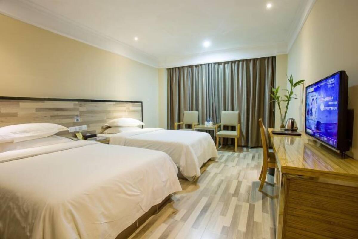 Une chambre d’hôtel avec deux lits, un bureau avec une chaise, une télévision et une grande fenêtre avec des rideaux.