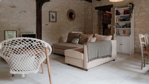 Uma sala de estar aconchegante com parede de pedra, um sofá branco, uma poltrona de vime e uma estante de livros.