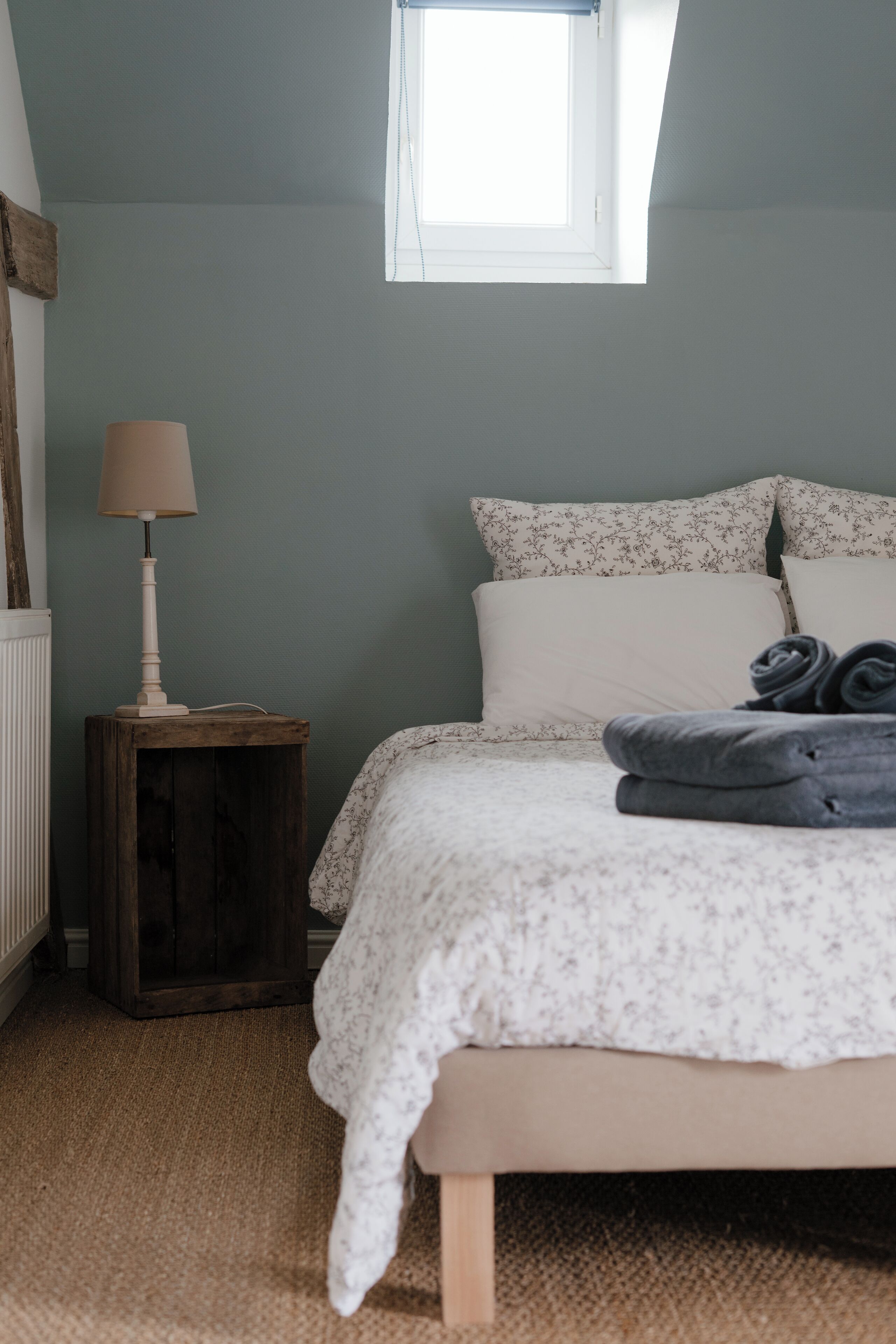 A bedroom with a bed, a nightstand, a lamp, and a window.
