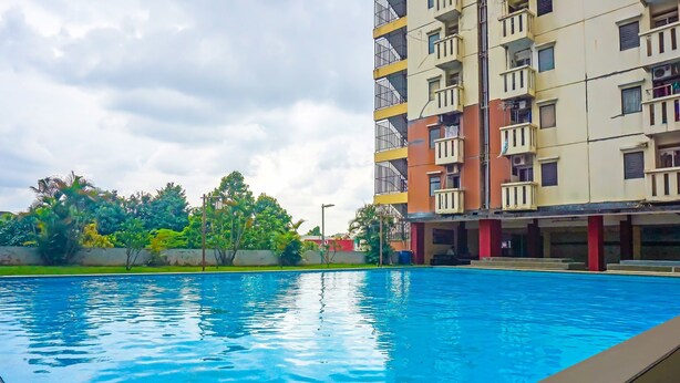 A swimming pool with a clear blue water surface, surrounded by a low wall. In the background, there is a multi-story residential building with balconies and windows. - OYO 92292 Nadjla Property Cibubur Village (Depok)