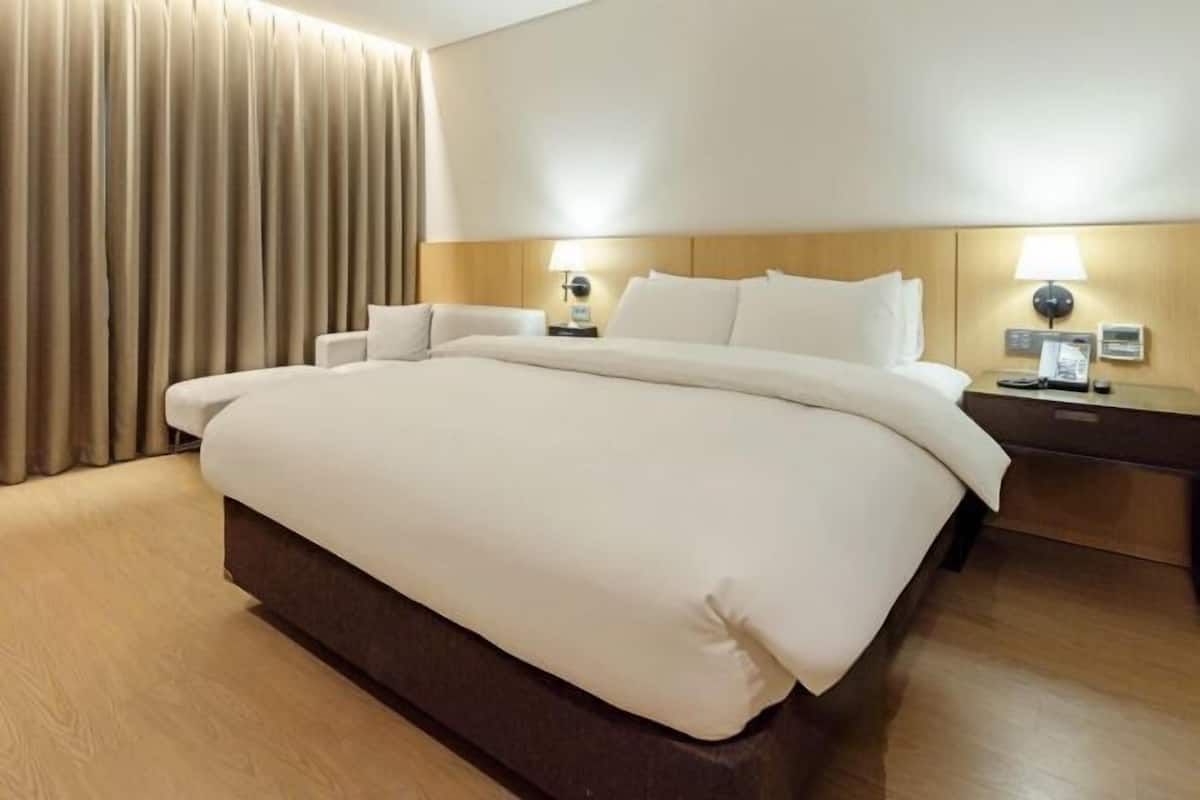 Una habitación de hotel con una cama grande, dos mesitas de noche con lámparas y una cortina en la ventana.