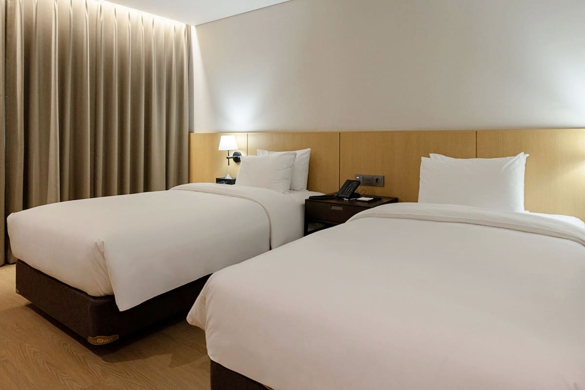 Una habitación de hotel con dos camas, una mesita de noche, una lámpara y un teléfono.