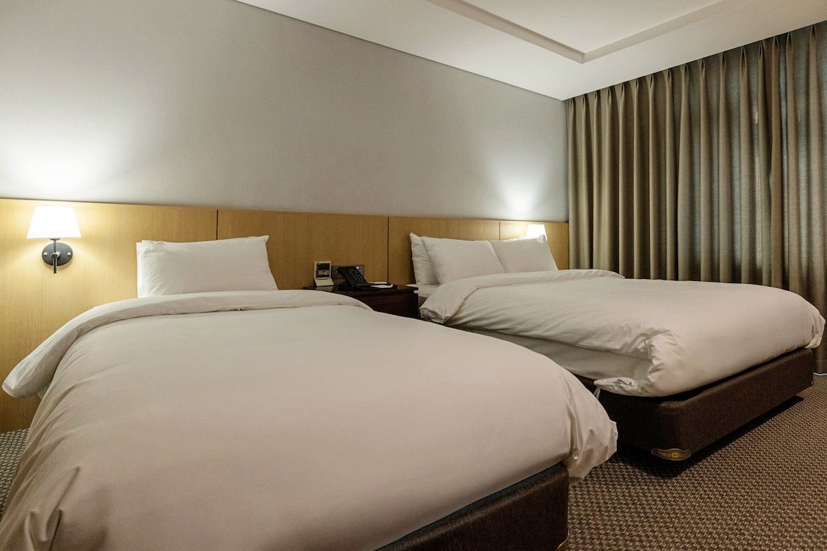 Una habitación de hotel con dos camas, una mesita de noche con lámpara y una cortina.