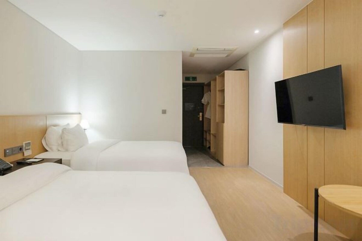 A hotel room with two beds, a television mounted on the wall, and a wooden wardrobe.