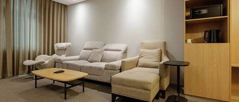 A hotel room with a sofa, armchair, coffee table, and a small side table.