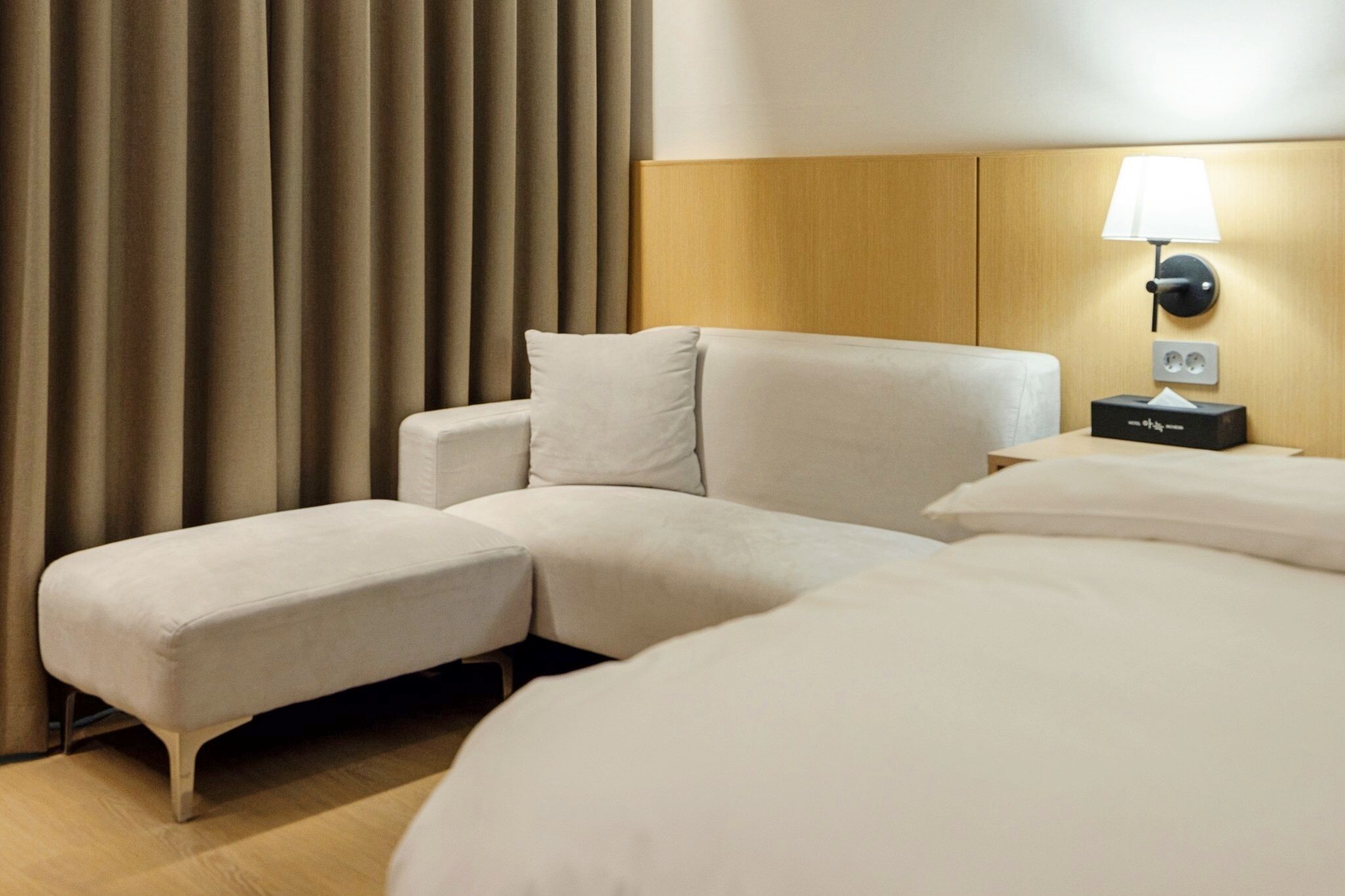 Una camera d'hotel con un letto grande, un divano letto, un comodino con una lampada e una tenda.
