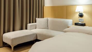 Una camera d'hotel con un letto grande, un divano letto, un comodino con una lampada e una tenda.