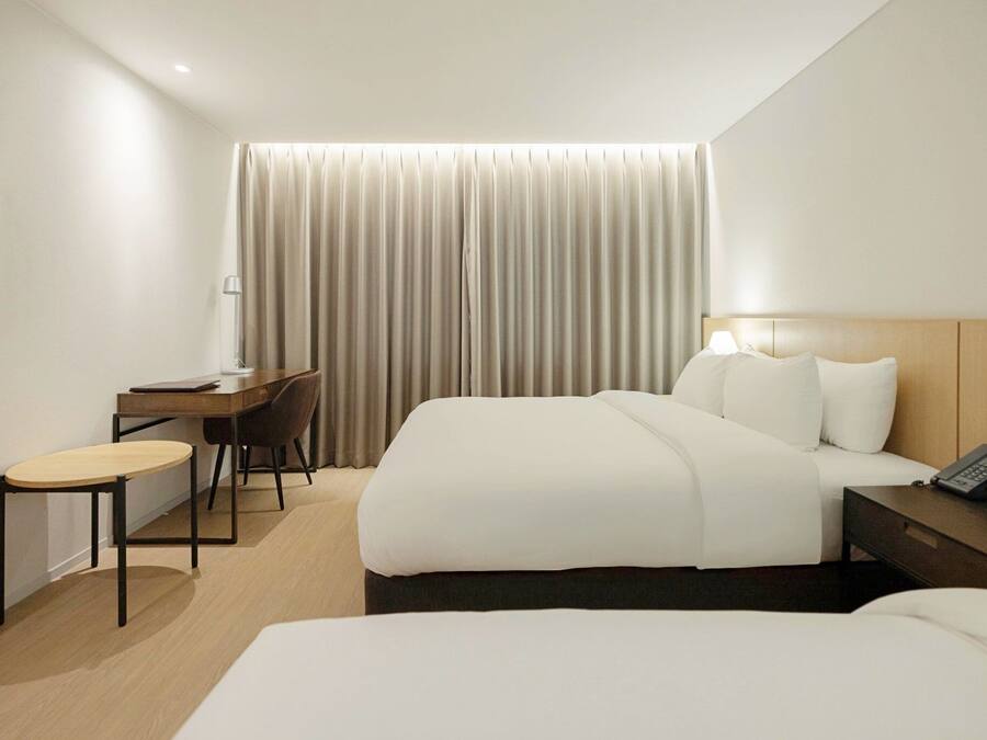 A hotel room with a bed, a desk, a chair, a lamp, and a telephone.