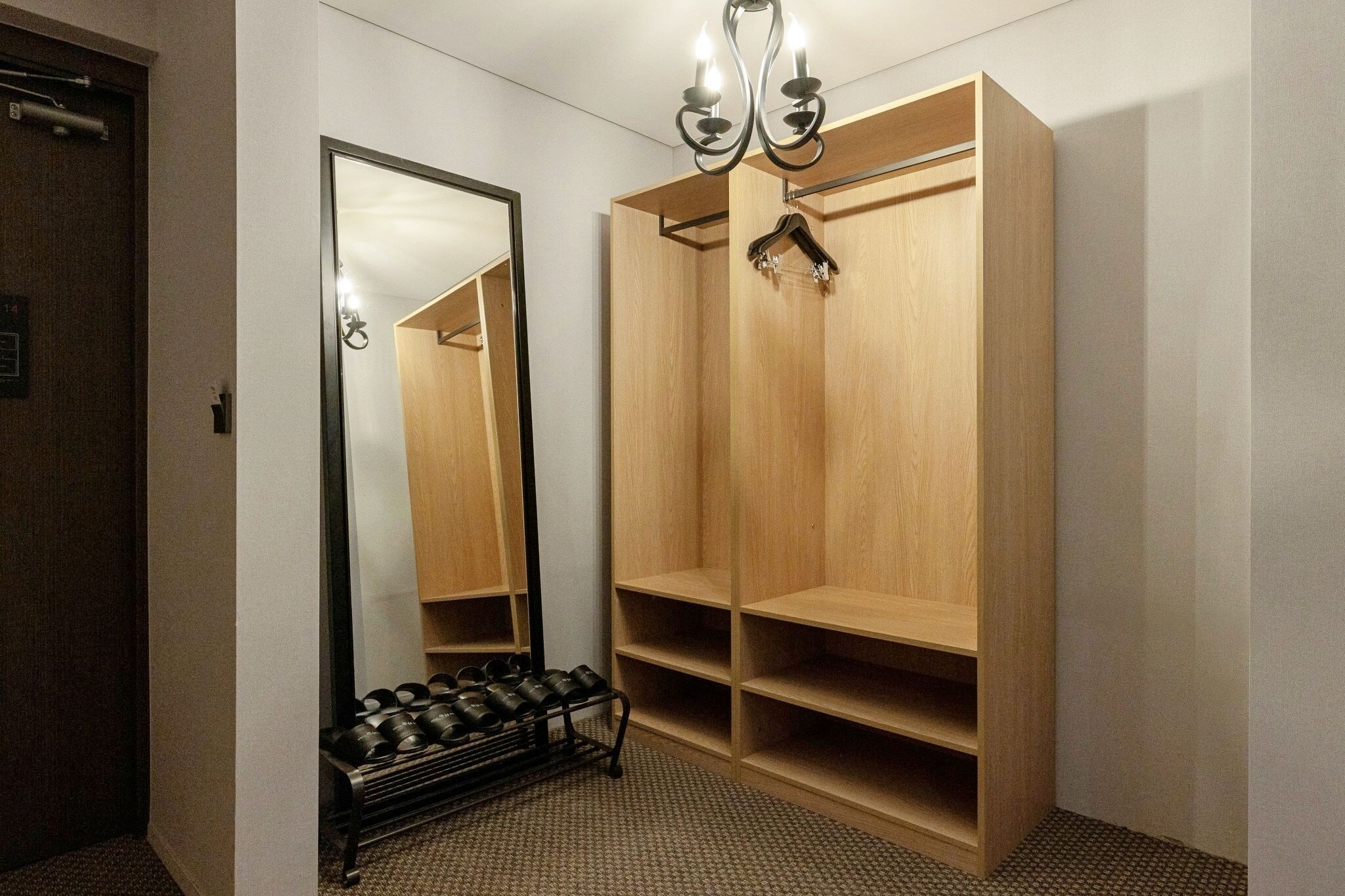 Een hotelkamer met een grote spiegel, een houten garderobe en een schoenenrek.