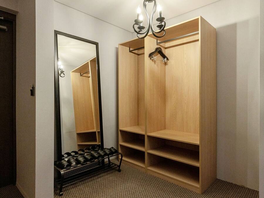 Een hotelkamer met een grote spiegel, een houten garderobe en een schoenenrek.
