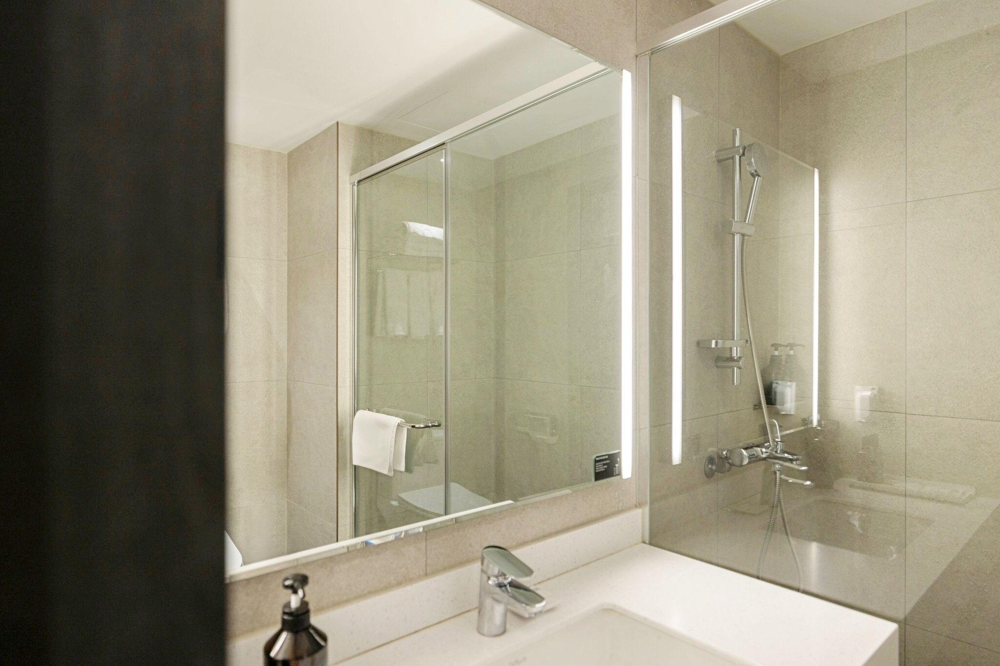 Une salle de bain moderne avec une douche à parois de verre, un grand miroir et un lavabo blanc.